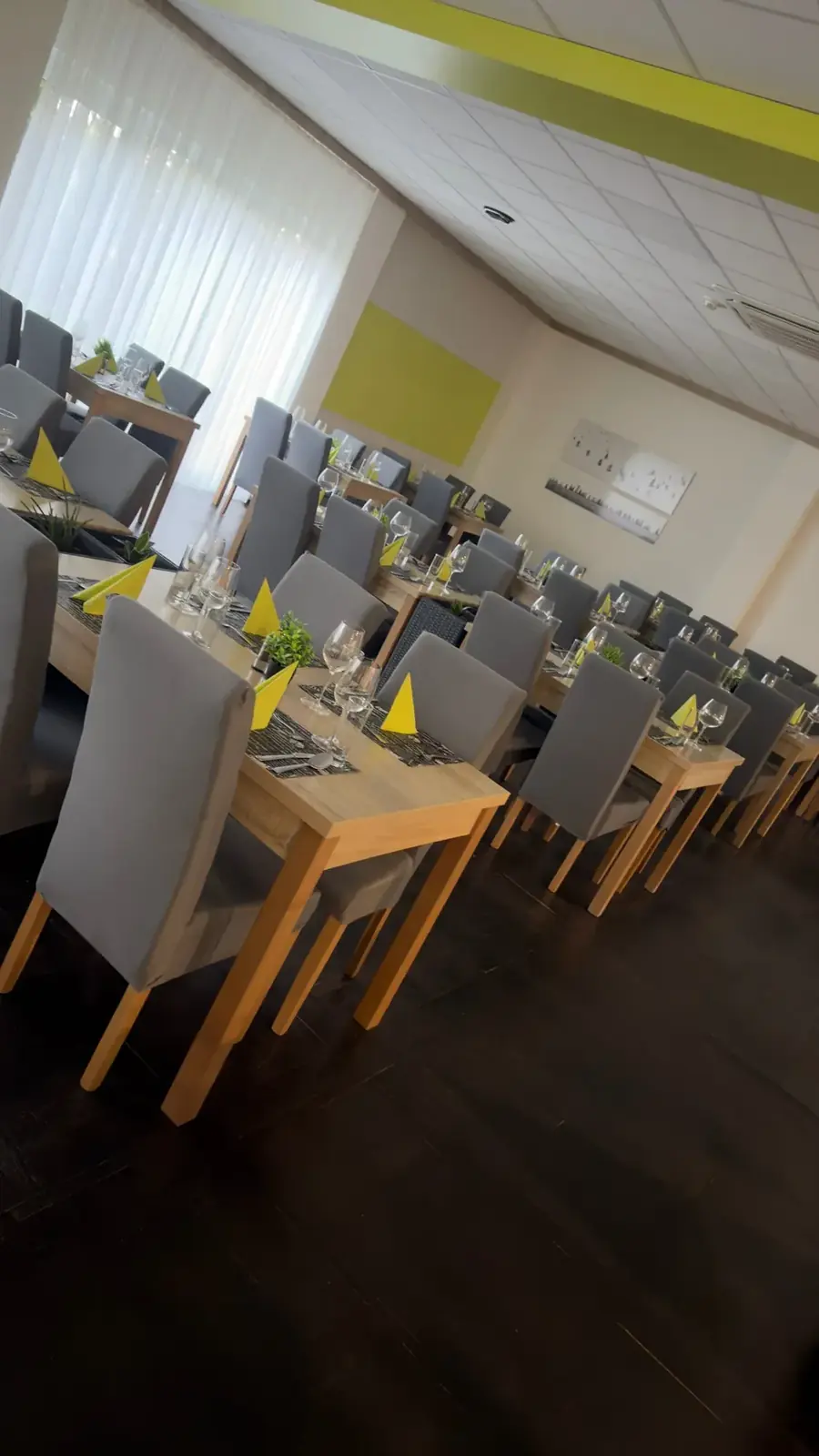Gedeckte Tische mit grauen Stühlen und gelbgrünen Servietten im Restaurant des Hotel Csopak
